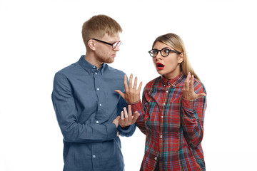 Stylish young European couple in glasses having arguement in studio: emotional blonde girl with fed up look, feeling tired and stressed while explaining her grumpy bearded husband thar she is right