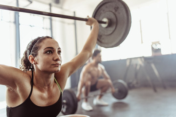 Tough young woman exercising with barbell