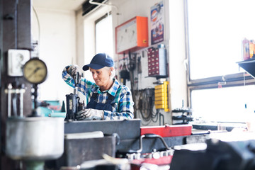 Senior female mechanic repairing a car in a garage.