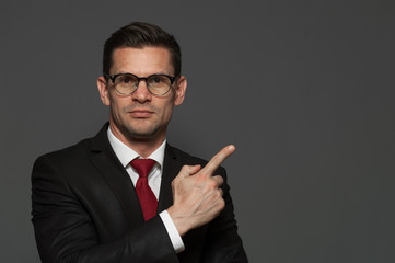 Portrait of successful young positive businessman pointing his finger at the space showing something useful on gray background