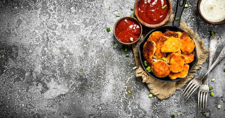 Chicken nuggets in a pan with different sauces.