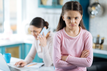 Miffed. Pretty resentful dark-eyed girl her arms crossed and sitting near her mom working on her laptop