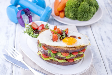 Toast from a grain bread with cheese and tomatoes and egg. Vegetarian food. on a white plate and blue dumbbells and a fitness bracelet for fitness. Useful breakfast. Free space for writing text.