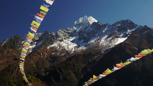 Multi-colored Buddhist flags ripple in the wind against the background of snow-capped mountains