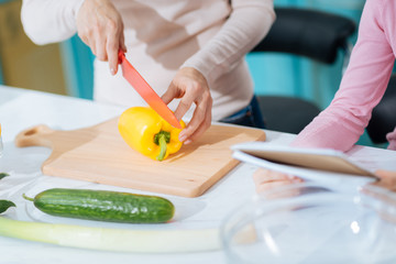 Making a salad. Loving caring devoted mother chopping a pepper on a chopping board and making a salad while her daughter standing near her