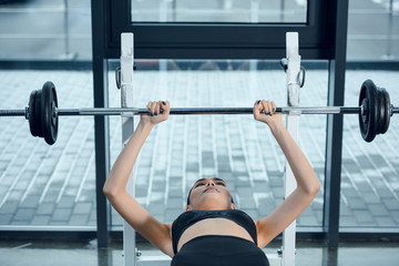 Fototapeta na wymiar young fit woman lifting barbell while lying on bench at gym