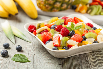 Delicious fruit salad with fresh fruit. Wooden, gray table in the background.