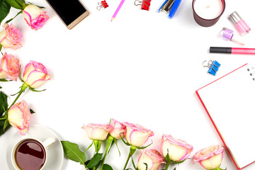 Beautiful feminine arrangement with pink roses, notebook with a blank page, cup of tea, mobile phone and other accessories. White background, copyspace