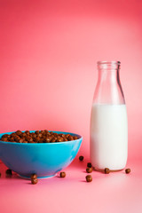 Plank milk in a glass bottle and chocolate breakfast cereals in a blue bowl on pink background. Selective focus