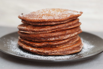 Holliday Breakfast. Chocolate Pancakes in Black Plate. Sugar Powder. LIght Background. Front View.