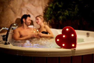 Heart on a background of a romantic couple with champagne in the jacuzzi. Valentines day. - obrazy, fototapety, plakaty