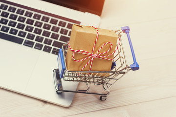 Shopping time. A laptop and shopping cart gift box wrapped with paper kraft on table.