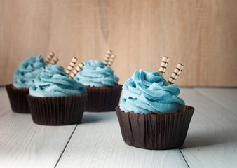 Four cupcakes with blue cream in brown paper form with two wafer tubules on a light background