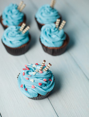 Five capkakes with blue cream with powder in the form of hearts and two wafer tubules in brown paper form on a light background