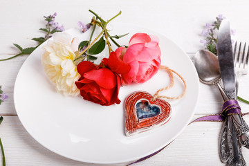 Festive table setting for Valentine's Day with cutlery, roses and hearts on white table. Space for text. Top view.