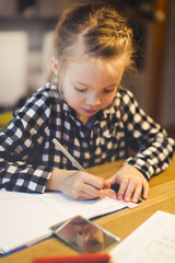 beautiful, blond girl is sitting at the table and is doing schoolwork at home