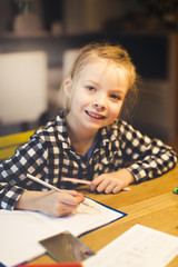 beautiful, blond girl is sitting at the table and is doing schoolwork at home
