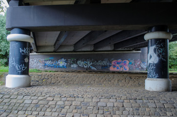 The underside of a steel road bridge which has had graffiti added to the support columns and brick wall