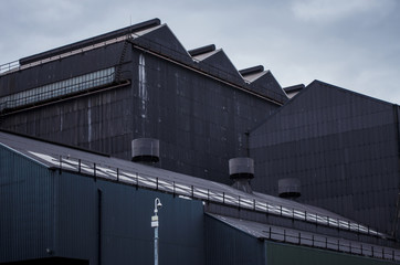 A group of dark grey factory buildings constructed from corrugated steel with a cctv security camera mounted on a pole © johndavidphoto