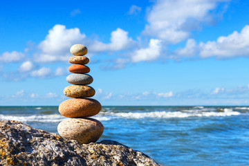 Pyramid of colored pebbles on the background of the summer sea and blue sky with Cumulus clouds