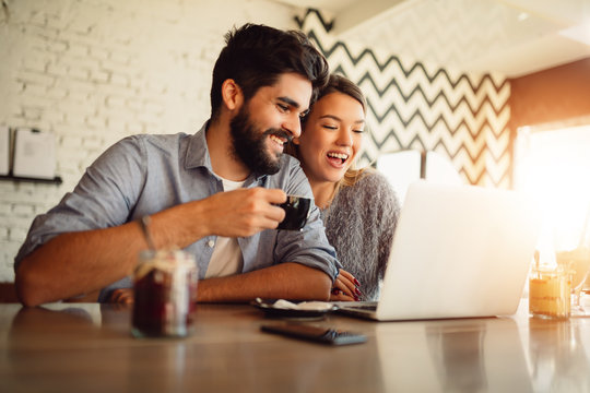 Happy Couple Surfing On A Laptop At Cafe. Couple Shopping Online Or Video Chatting.