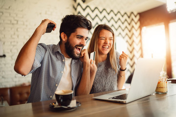 Couple doing online shopping through laptop and credit card at cafe.