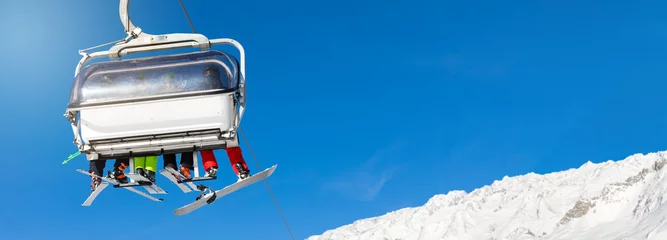 Fotobehang skiers and snowboarders in a ski lift against clear blue sky. blank space for text © ronstik