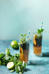 Two Glasses of classic Cuba libre cocktail with lime, mint, crushed ice and cola, served with ingredients above and retro cocktail tubes over turquoise green pin-up style background. Sunlight, space
