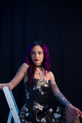 Naklejka premium Beautiful Girl Dyed Hair Tattooes Posing Studio Dark Wall Chair