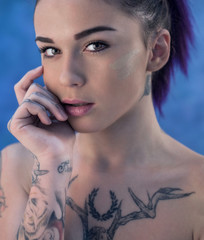 Beautiful girl with dyed hair and tattooes posing in studio on blue background