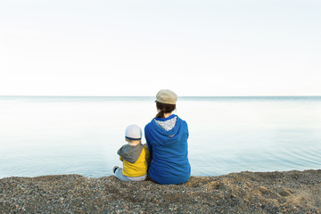 Mother or sister with child looking at sea far away and sitting on shore