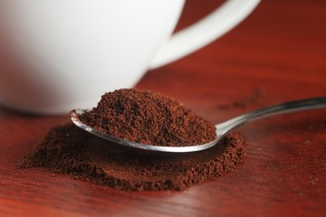 A spoonful of ground coffee lies on the table. Against the backdrop of a cup. Dark kitchen In a low key. Close-up. Macro