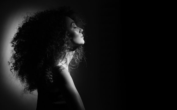 beautiful girl with curly hair on a black background looking to the side, her eyes closed, black and white photo