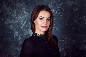Portrait of beautiful young smiling  brunette woman, wearing black blouse, standing behind dark...