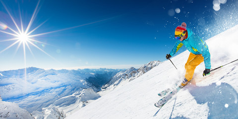 Skieur sur piste en descente dans un magnifique paysage alpin. Ciel bleu sur fond.