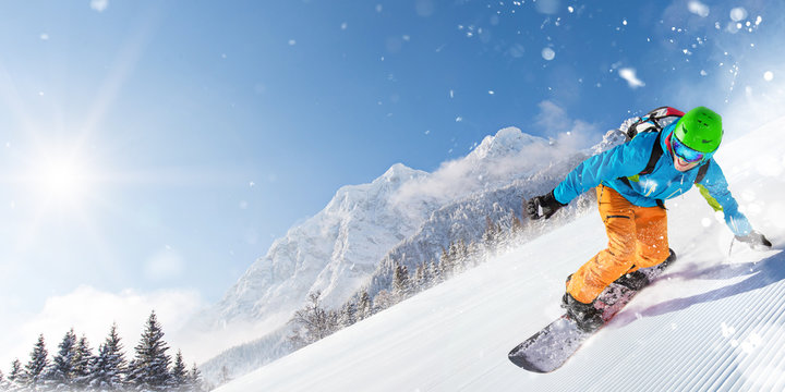 Snowboarder on piste running downhill in beautiful Alpine landscape. Blue sky on background.