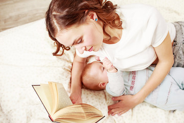 Young woman wearing white t-shirt reading a book while brestfeeding a baby on bed