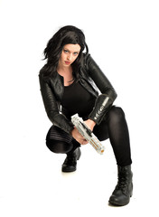 full length portrait of black haired girl wearing leather outfit. sitting pose, isolated on a white studio background.