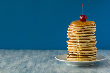Stack of pancakes with honey decorated sweet cherry on blue background