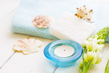 Obraz na płótnie Canvas Aromatherapy Spa Concept with a fragrant candle in a blue candle holder, a bar of soap, terry towels, sea shells and white flower on white wooden background