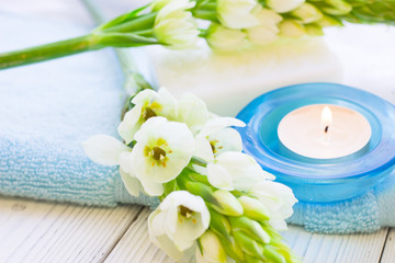 Obraz na płótnie Canvas Aromatherapy Spa Concept with a fragrant candle in a blue candle holder, a bar of soap, terry towels and white flower on white wooden background, selective focus