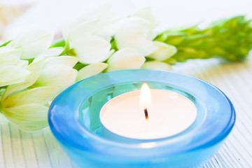 Aromatherapy Spa Concept with a fragrant candle in a blue glass candle holder, and beautiful white flower on white wooden background, close up
