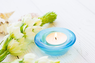 Obraz na płótnie Canvas Aromatherapy Spa Concept with a fragrant candle in a blue glass candle holder, and beautiful white flower on white wooden background, close up