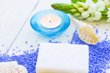 Spa Treatment Concept mock up with natural lavender bath salt, an aroma candle in a blue candle holder, white flowers, a bar of soap and sea shells on a white wooden table , top view