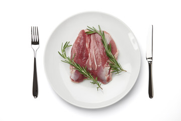 Raw duck fillet with rosemary in big round plate and cutlery isolated on white background, top view