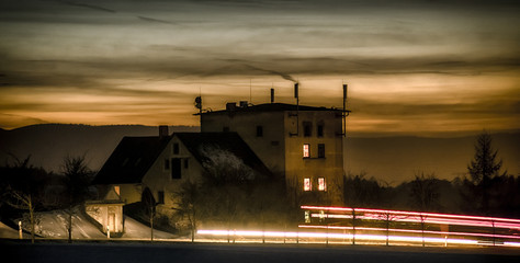 The old mill stands quietly in the evening light, its blades still. Bathed in the golden glow of the sunset, it casts long shadows across the field as the last rays of the sun paint the sky a warm 