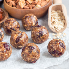 Healthy homemade energy balls with cranberries, nuts, dates and rolled oats on a parchment, square format