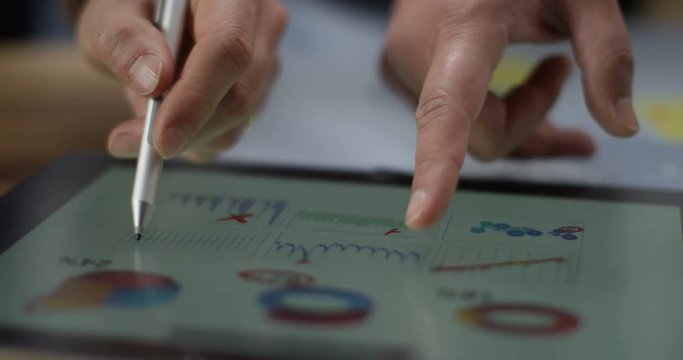 4K Extreme close up of computer tablet showing financial data, anonymous business team in a meeting. Slow motion.