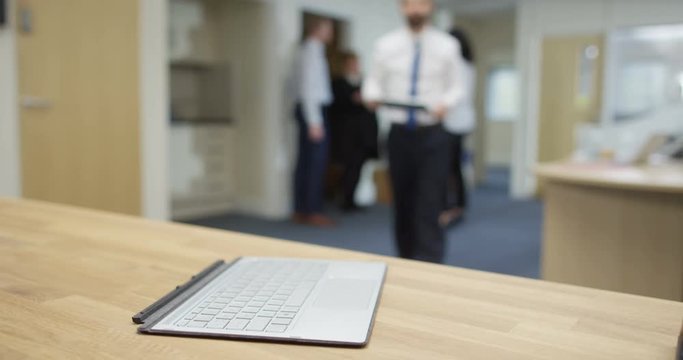 4K Businessman attaches tablet screen showing financial graphs to its keyboard & blurred business group shaking hands on a deal in background. Slow motion