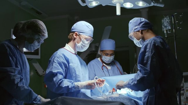 Medium shot of surgeon with suction tube removing blood from incision area during operation